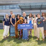 A group of people and a costumed Nittany Lion pose for a photo in front of Penn State Health Golisano Children’s Hospital, many of them smiling and pointing, “goofy pose” style. They hold a large sign that reads “Thank You!”