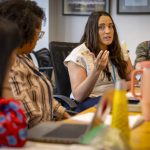 Joanie Miller gestures during a discussion at a table while three other people look on