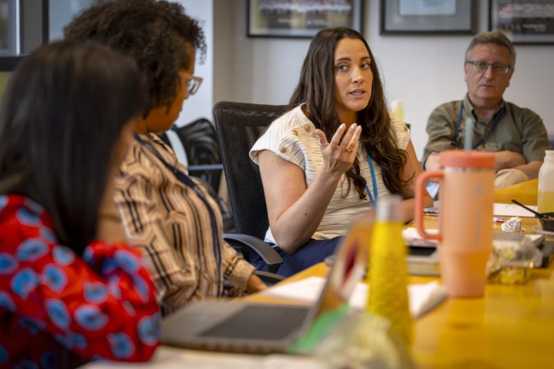 Joanie Miller gestures during a discussion at a table while three other people look on