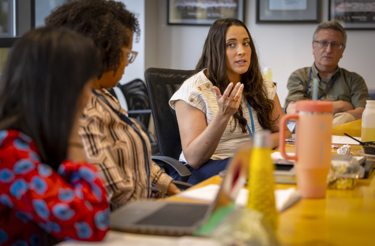 Joanie Miller gestures during a discussion at a table while three other people look on