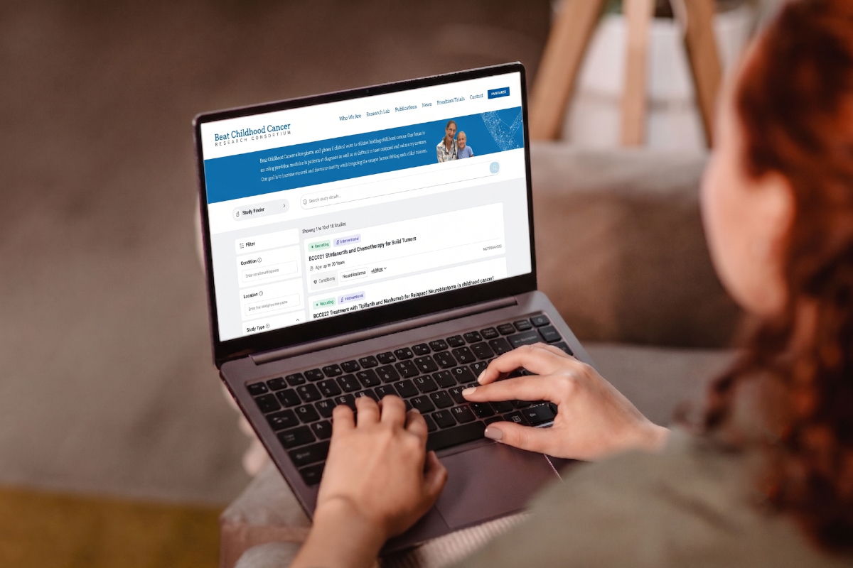 A view from over the shoulder of a woman typing on a laptop computer. On the screen is a page within the Beat Childhood Cancer Research Consortium website that displays Study Finder search results.