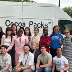 A group of diverse students stands together in front of a Cocoa Packs van.