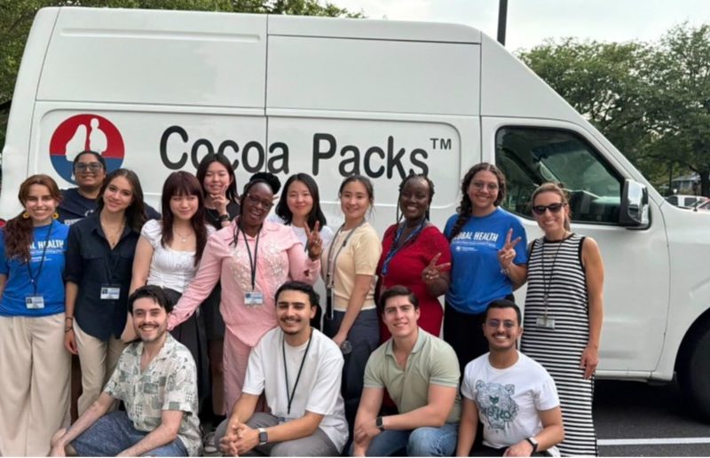 A group of diverse students stands together in front of a Cocoa Packs van.