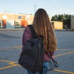 Person with a backpack walks alone in a school courtyard