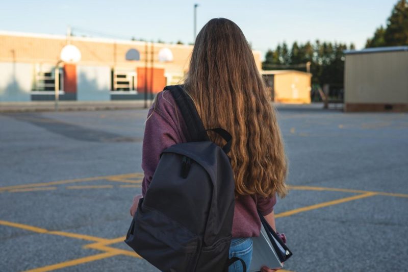 Person with a backpack walks alone in a school courtyard