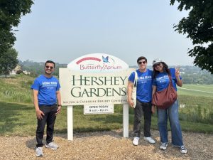 Three students stand beside a sign for the Hershey Gardens.