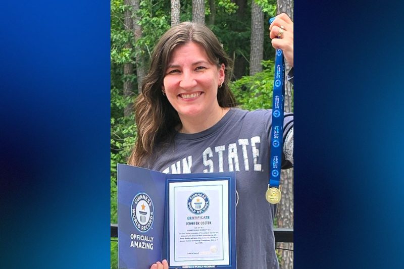 A woman holds a medal and certificate in front of trees.