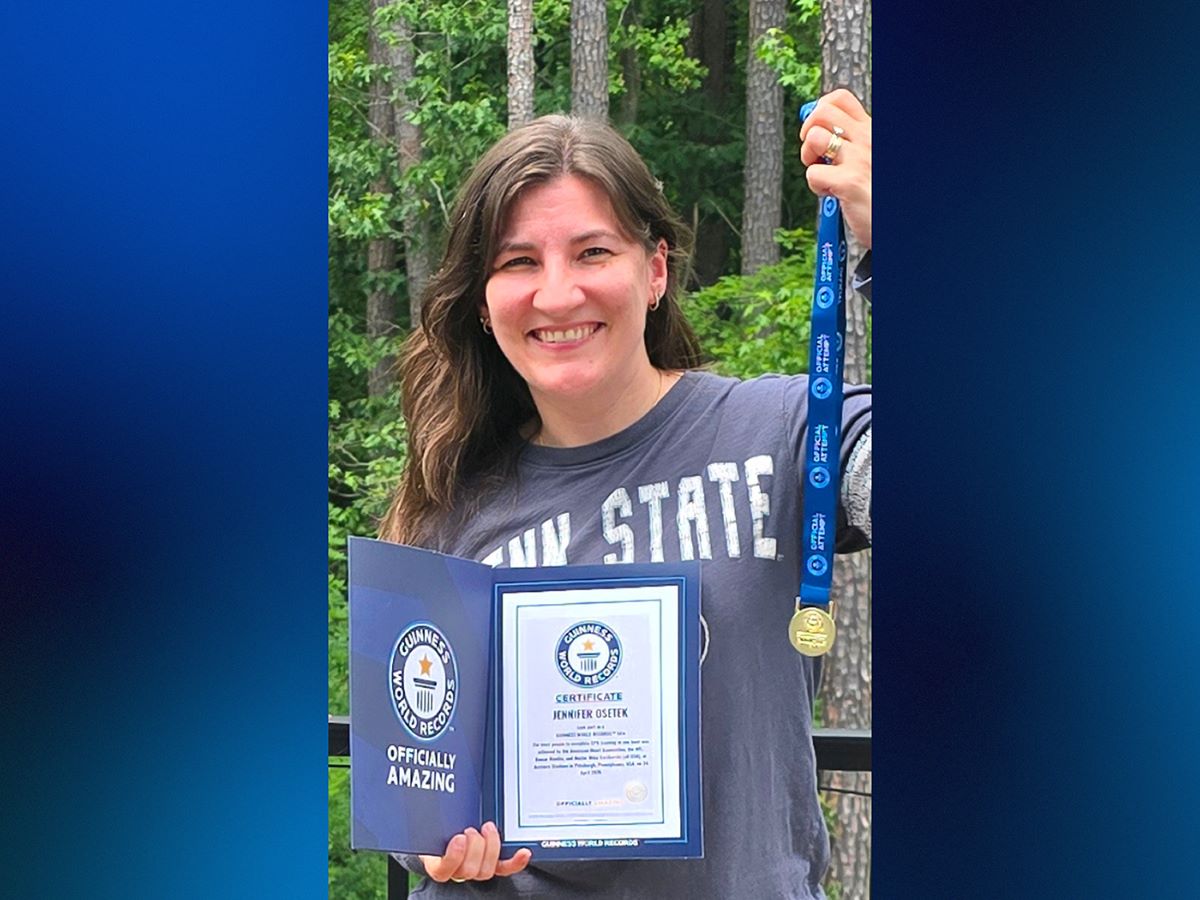 A woman holds a medal and certificate in front of trees.