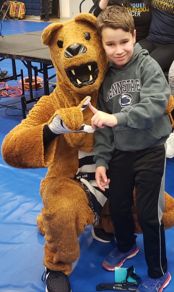 A child wearing a Penn State sweatshirt poses with the Penn State Nittany Lion mascot.