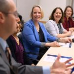Penn State Clinical and Translational Science Institute leadership and scholars smile and listen attentively to a colleague speak during a meeting in a conference room.