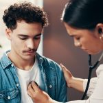 A doctor checks a young adult patient's heart with a stethoscope.