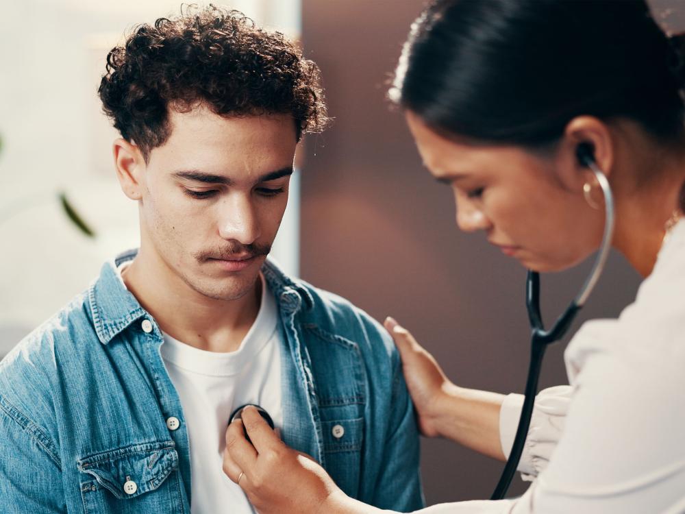 A doctor checks a young adult patient's heart with a stethoscope.
