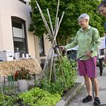 Laurie Funk, left, director of the Chestnut Street Community Center in Lebanon, holds a hose and waters a garden filled with lettuce and other produce. Laurie Crawford, Penn State Health program manager for food access, stands next to her.