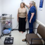 A woman gets her height measured by a medical assistant in a doctor’s office.
