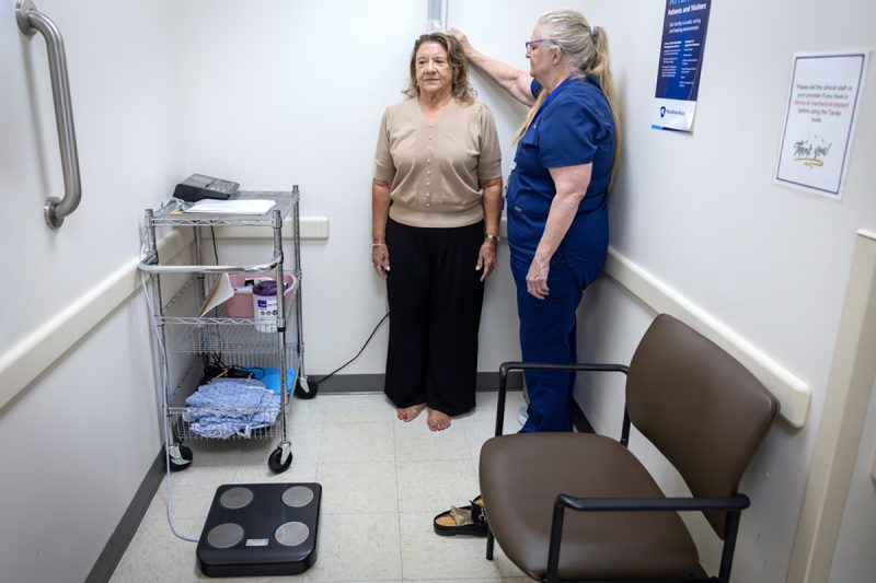 A woman gets her height measured by a medical assistant in a doctor’s office.