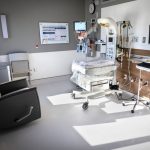 Bright, private neonatal intensive care unit (NICU) room at Penn State Health Lancaster Medical Center featuring an infant warmer with monitoring equipment, IV pumps, overhead exam light, bedside computer workstation, and a reclining chair for parents.