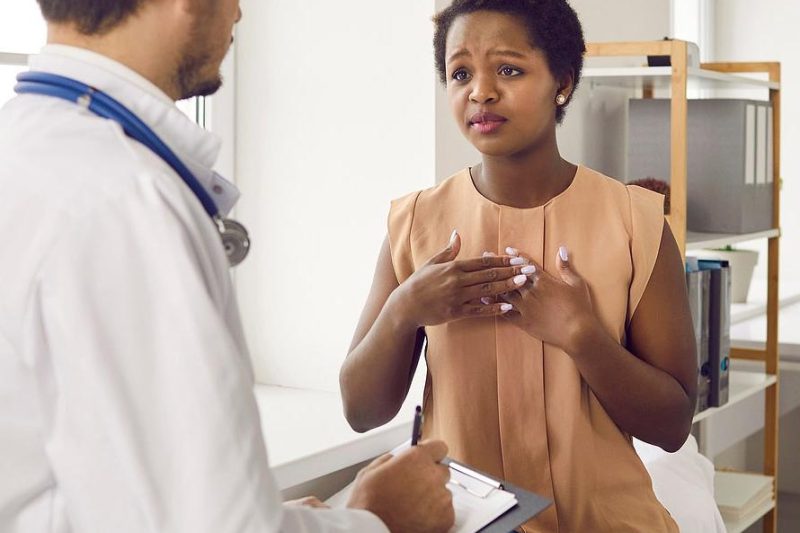 A patient sitting in a medical exam room, speaking earnestly with a doctor who is taking notes on a clipboard.
